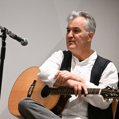 Timothy Hill, seated, holding an acoustic guitar.