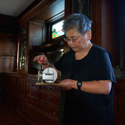 Susie Kozawa holding a small mechanical object in a room with dark wood and stained glass.