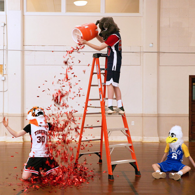 Three people dressed as mascots, one standing and dumping confetti on another on the left, while a third sits watching on the right.