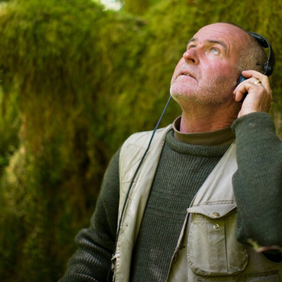 Gordon Hempton wearing headphones with a green, mossy background.