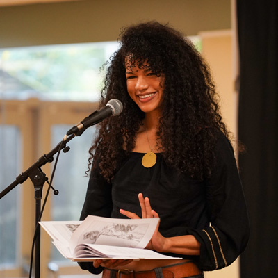 Arami Walker standing at a microphone, holding a book.