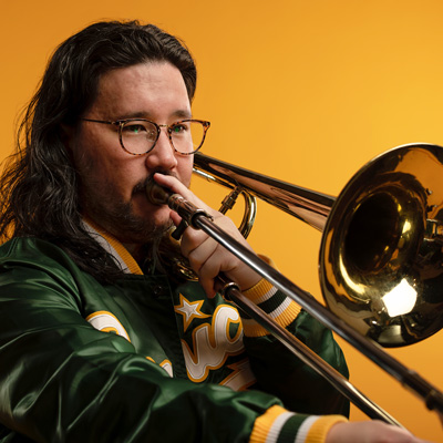 Greg Kramer playing the trombone, with a yellow background.