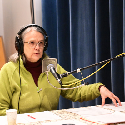 Julene Tripp Weaver, seated at a table in front of a microphone, wearing headphones.