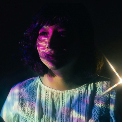 Photo of Laura Luna Castillo in a dark space with colorful projections on her face and shirt.