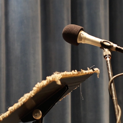 A microphone on a stand next to a music stand, with a background of blue-gray curtains