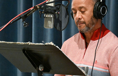 Stacy Nathaniel Jackson, standing at a music stand and microphone, wearing headphones.
