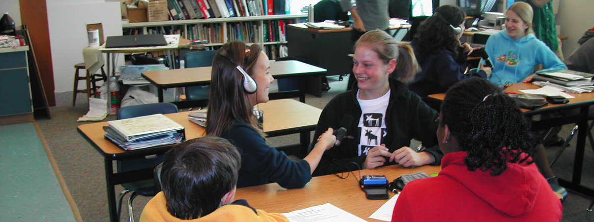 Students interviewing each other in a classroom with headphones and microphones