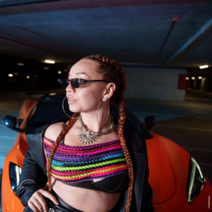 KTNA, in front of an orange sports car in an underground garage.