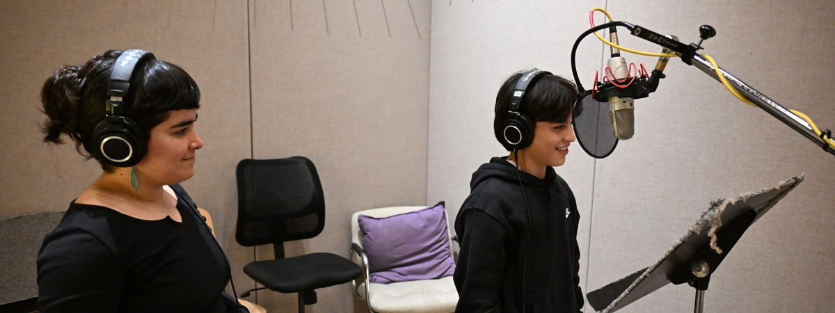 Vocal coach and Denny student wearing headphones in a recording studio with a microphone.