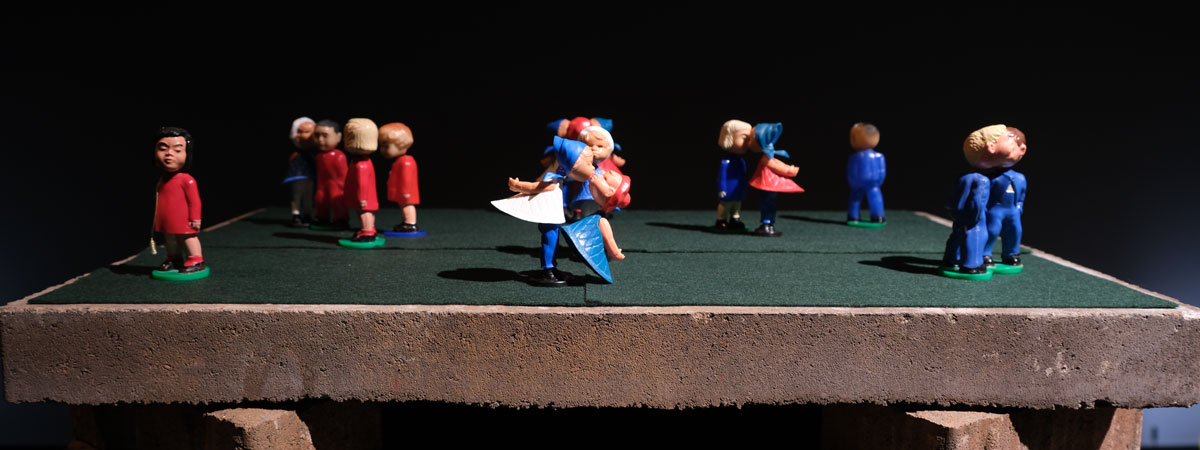 Toy figures of people in red and blue on a green surface with brick below it.