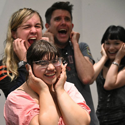 Four people covering their ears and singing or shouting.