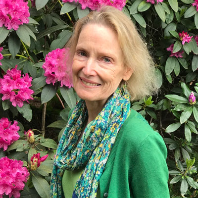 Laura Ferri, standing in front of a rhododendron with bright pink flowers.