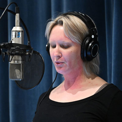 Asha Dore, wearing headphones, speaks into a microphone.