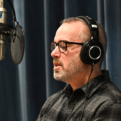 Bill Hollands speaks into a microphone, wearing headphones.