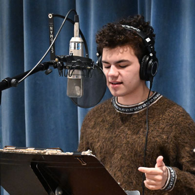 Mateo Bracken wears headphones and speaks into a microphone.