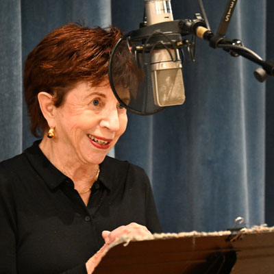 Sigrun Susan Lane, smiling, standing at a microphone.