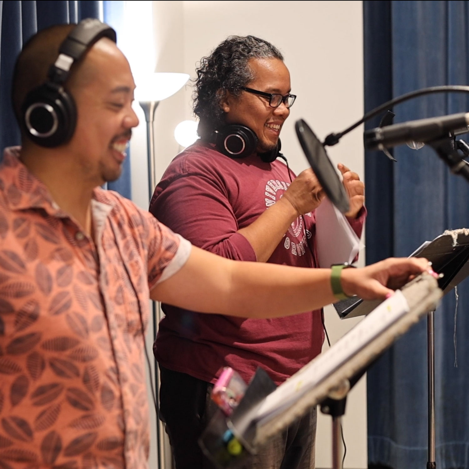 Two people stand at microphones, smiling and wearing headphones