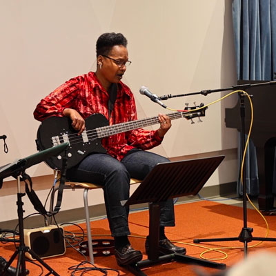 LaVon Hardison, seated with a microphone in front of her, plays the bass and sings.