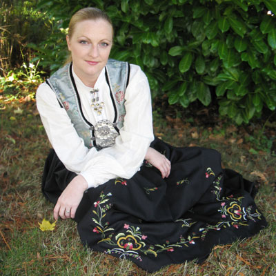 Laura Loge, in traditional Scandinavian clothing, sits in the grass.