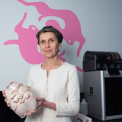 Timea Tihanyi stands next to a 3D printer holding a sculpture.