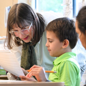 Vicky Edmonds and a student look at a piece of paper. A hand in the foreground holds a pencil.