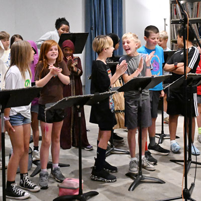 Students smiling and clapping in a recording studio with music stands.