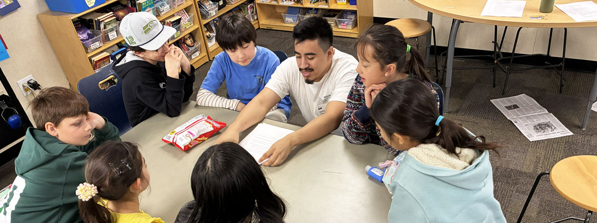 Carlos and seven students seated around a table looking at a piece of paper.
