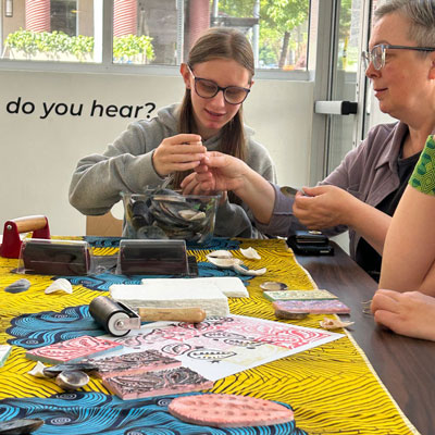 A youth and adult sit a table with colorful prints and art supplies