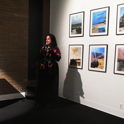 River stands in a gallery space in front of six framed prints on a white wall.
