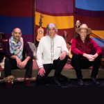 Tony, Gus, and Abel seated on a stage with musical instruments and a colorful backdrop behind them.