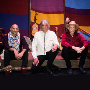 Tony, Gus, and Abel seated on a stage with musical instruments and a colorful backdrop behind them.