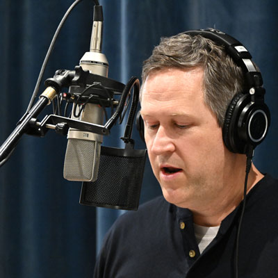 Kevin Dean wearing headphones, speaking into a microphone.