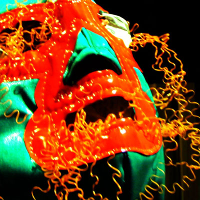 High contrast image of a green and orange lucha libre mask with twisting orange fibers around it.