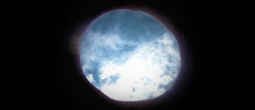 Black background, with a rough circle in the middle showing blue sky and white clouds