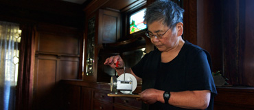Susie Kozawa holding a small mechanical object in a room with dark wood and stained glass.